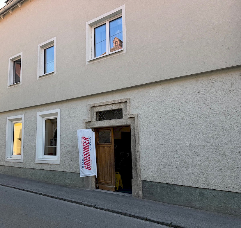 Eingang SPECIALISTA im Gutmannhaus an der Leitenstraße in Lambach, mit Grassinger-Fahne neben der Holztür